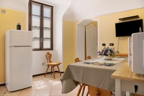 Una cocina compacta con refrigerador, una mesa de comedor con sillas, un florero y un televisor montado en la pared.