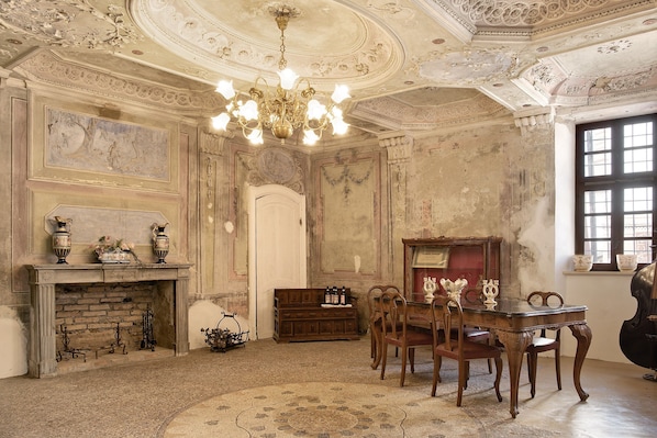 A room with a fireplace, a chandelier, a wooden table with chairs, and a piano.