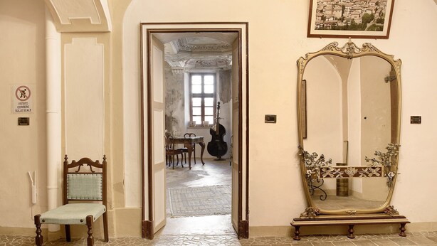 A hallway with a chair, a mirror, and a door leading to another room.