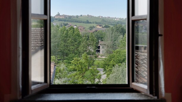 Una vista attraverso una finestra su una zona residenziale, con case, alberi e una collina all'orizzonte.