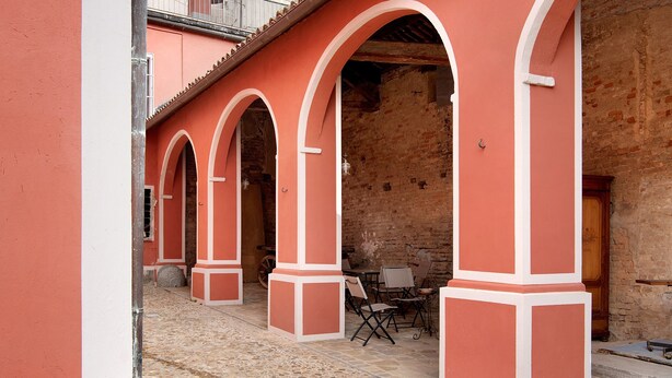 A building with red walls and white trim, featuring a courtyard with tables and chairs. - Apartment 'La Rocca di Efisio - Barbera with Private Terrace, Wi-Fi and Air Conditioning (Costigliole d'Asti)