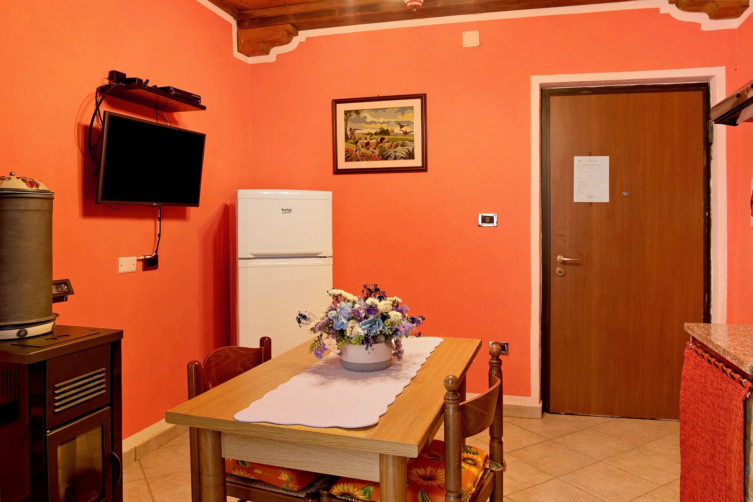 A kitchen with a wooden table, a white refrigerator, a television mounted on the wall, and a door with a note on it.
