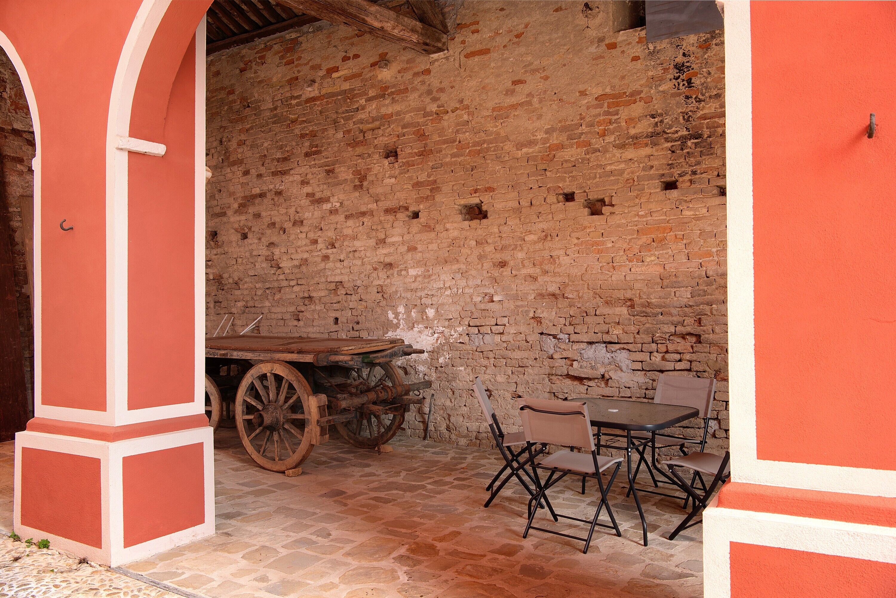 A rustic interior with a brick wall, a wooden cart, and a table with chairs.