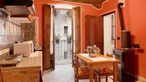 A kitchen with a stove, a microwave, and a sink. There is a dining table with chairs and a vase of flowers. A wood-burning stove is visible in the corner. - Apartment 'La Rocca di Efisio - Barbera with Private Terrace, Wi-Fi and Air Conditioning (Costigliole d'Asti)