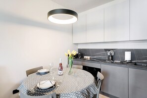A modern kitchen with a round dining table, a vase with yellow flowers, and a hanging light fixture.
