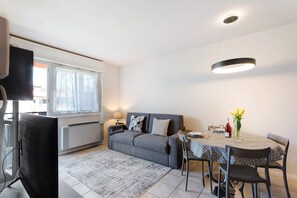 Una sala de estar moderna con sofá, mesa de comedor, sillas, televisor de pantalla plana y ventana con cortinas.
