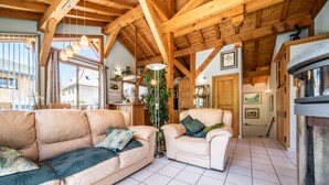 A cozy living room with a wooden ceiling, a sofa, a chair, a fireplace, and a view of the outside. - Chalet for 4 in Morzine with Mountain View, Private Terrace, and Wi-Fi (Morzine)