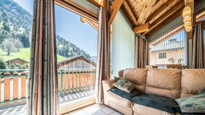 A room with a leather sofa, a view of a wooden cabin, and a balcony with a wooden railing. - Chalet for 4 in Morzine with Mountain View, Private Terrace, and Wi-Fi (Morzine)