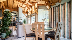 A wooden dining table with chairs, a potted plant, and a modern sofa in a room with wooden beams and large windows. - Chalet for 4 in Morzine with Mountain View, Private Terrace, and Wi-Fi (Morzine)