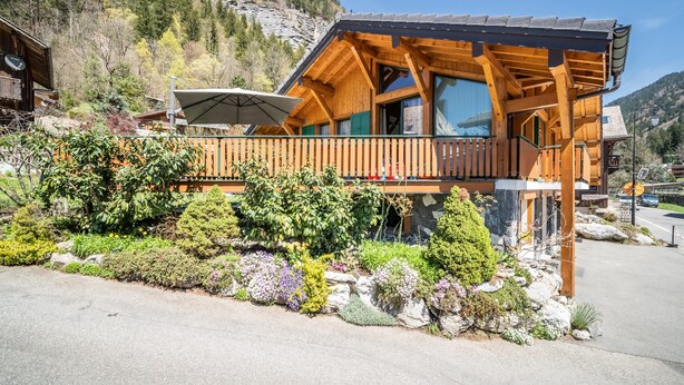 A wooden cabin with a balcony, surrounded by a landscaped garden with various plants and flowers. - Chalet for 4 in Morzine with Mountain View, Private Terrace, and Wi-Fi (Morzine)