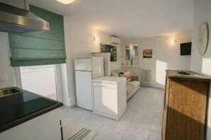 A compact kitchen with a refrigerator, a dishwasher, and a stove. There is a small seating area with a sofa and a coffee table. - Penthouse in Residential Area Near Trastevere with Terrace and Private Parking (Roma)