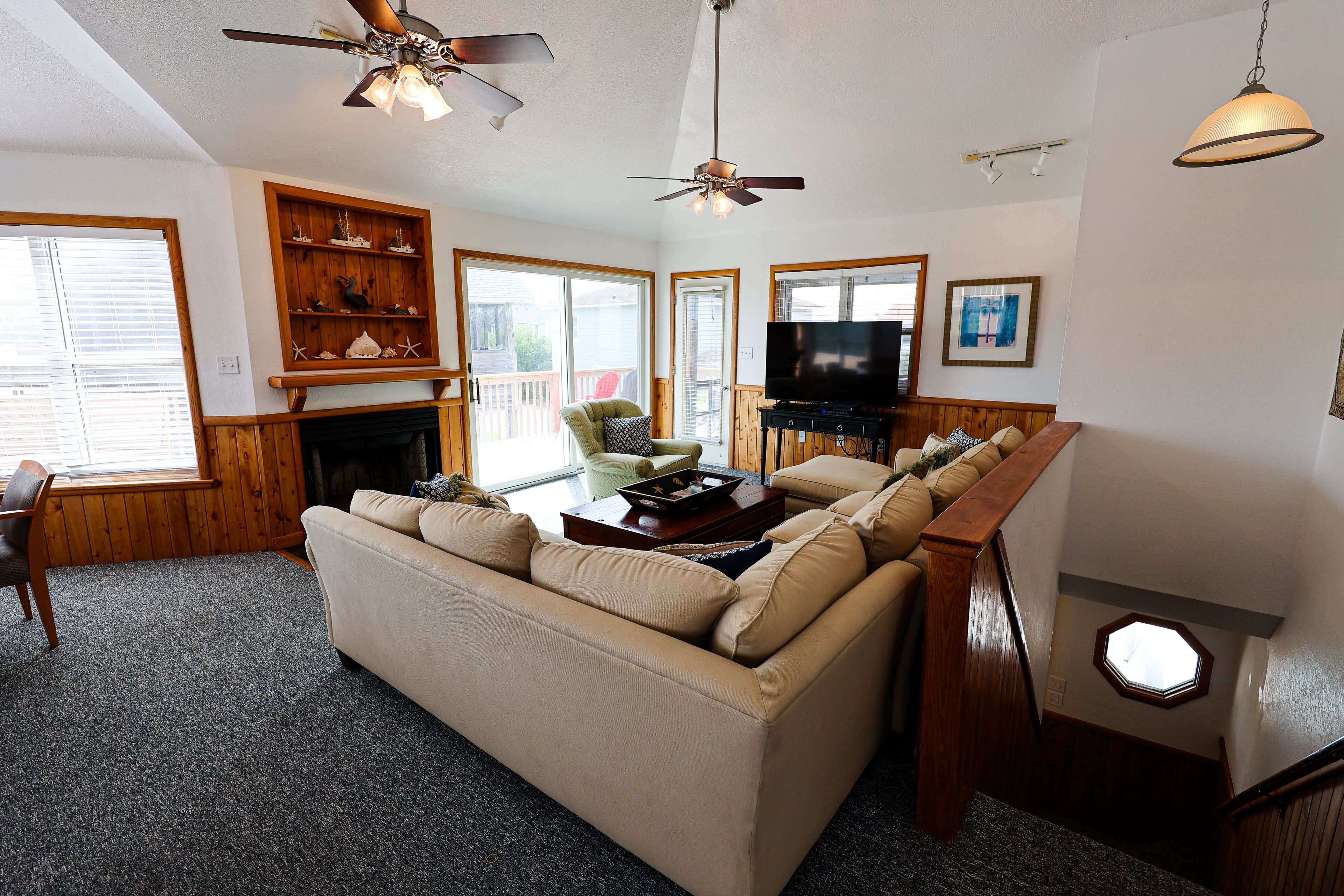 A living room with a beige sofa, wooden shelves, a television, and a ceiling fan.