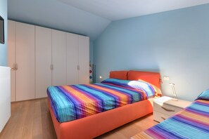 A bedroom with a bed, a nightstand, a wardrobe, and a wall-mounted shelf.