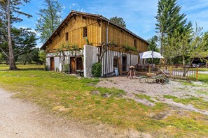 Un bâtiment rustique en bois, avec une cour en terre battue, une balançoire et un espace abrité.