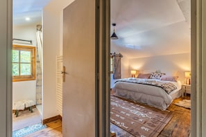 Une chambre à coucher avec un lit, des lampes de chevet, une fenêtre, un plancher en bois et une porte.
