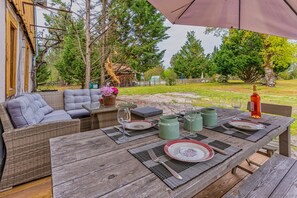 Un espace de restauration en plein air avec une table en bois prévue pour quatre personnes, entourée de meubles en osier et d’un grand parasol.