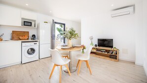 A modern kitchen with a washing machine, a dining table with chairs, a TV, and a bookshelf. - Apartment 'White Suites' with Shared Pool, Wi-Fi and Air Conditioning (Cala D'or)