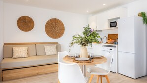 A modern kitchen with white cabinets, a white refrigerator, and a dining area with a wooden table and white chairs. - Apartment 'White Suites' with Shared Pool, Wi-Fi and Air Conditioning (Cala D'or)