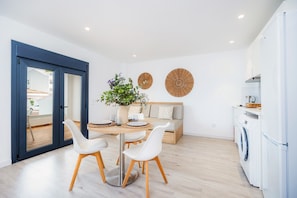 A modern kitchen with a built-in washing machine, a dining area with a round table and white chairs, and a living area with a sofa and a large plant. - Apartment 'White Suites' with Shared Pool, Wi-Fi and Air Conditioning (Cala D'or)