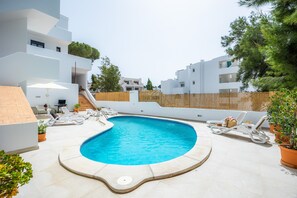 Una piscina rodeada de edificios blancos, mobiliario exterior y plantas en macetas.