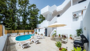 A modern outdoor pool area with lounge chairs, a barbecue grill, and potted plants. - Apartment 'White Suites 2' with Shared Pool, Wi-Fi and Air Conditioning (Cala D'or)