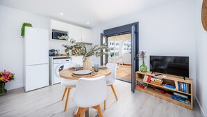 A modern kitchen with white appliances, a dining area with a round table and chairs, and a TV stand with books. - Apartment 'White Suites 2' with Shared Pool, Wi-Fi and Air Conditioning (Cala D'or)