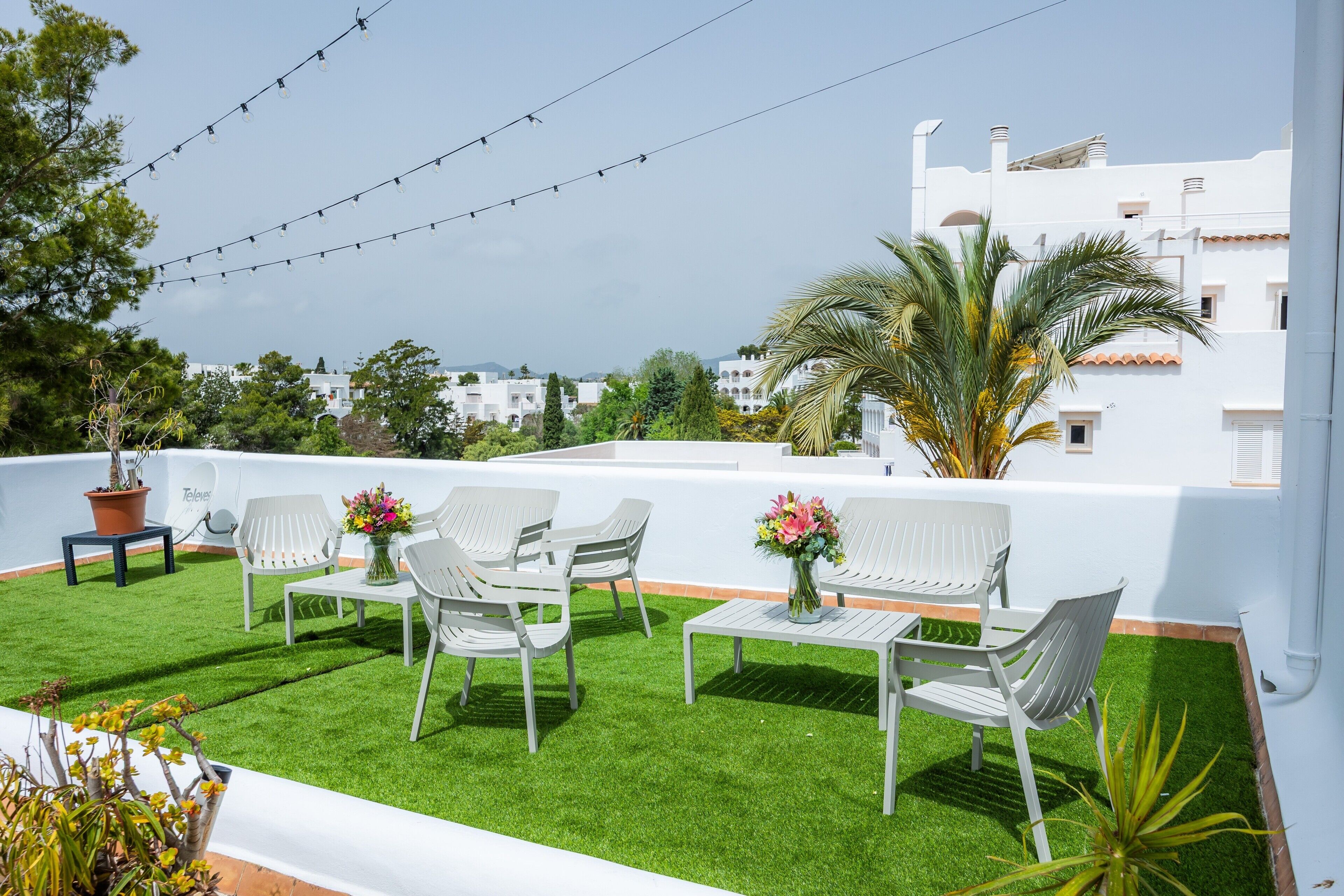 Eine Dachterrasse mit weißer Gartenmöbel, einem kleinen Tisch mit Blumenvase und Lichterketten.