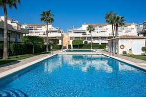 A swimming pool with a clear blue water, surrounded by buildings with balconies and palm trees.