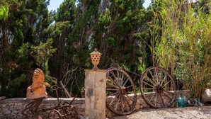 A stone pillar with a lion statue, two large wooden wheels, and a rustic setting with trees and greenery. - Studio Sur – Adults Only in Mallorca with Shared Pool (Manacor)