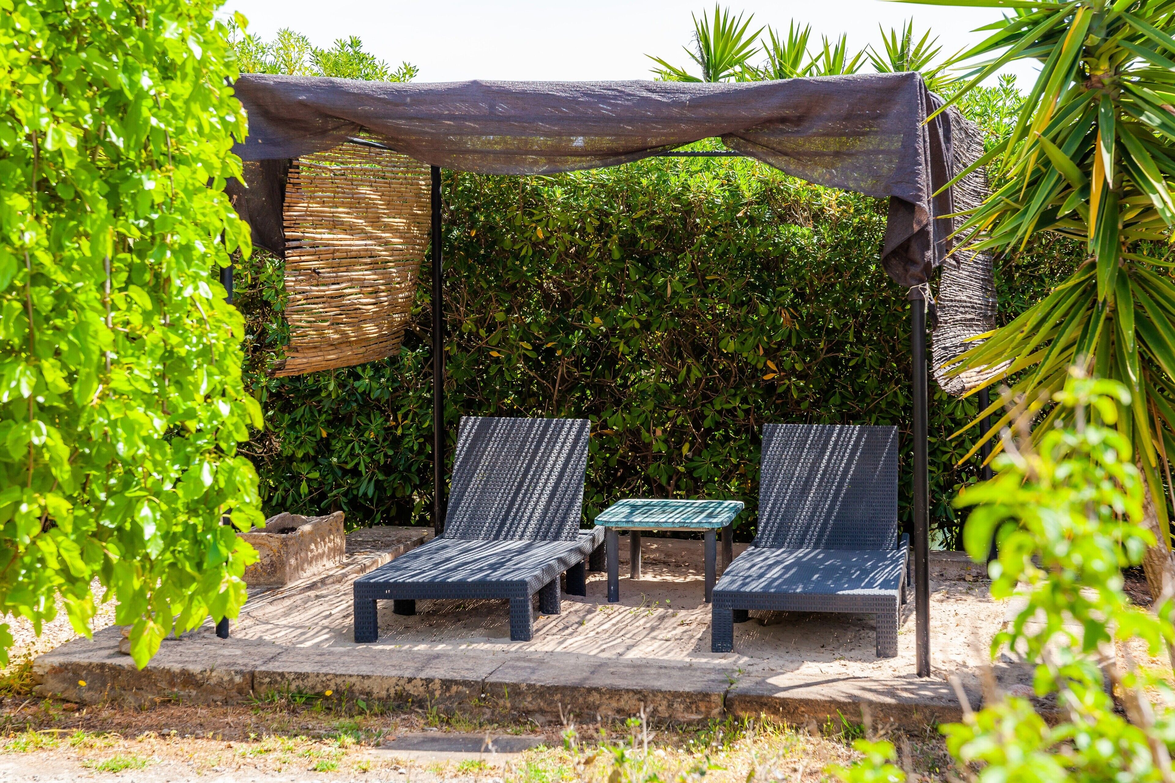 A covered outdoor seating area with two lounge chairs and a small table.
