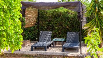 A covered outdoor seating area with two lounge chairs and a small table.