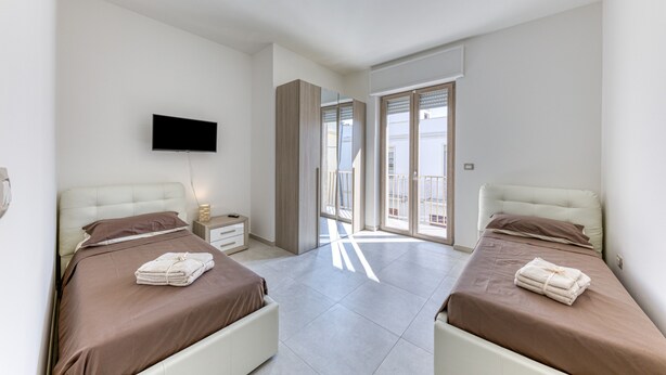 Een slaapkamer met twee bedden, een televisie, een nachtkastje en een balkon.