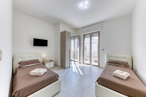 Et soveværelse med to senge, fjernsyn, et natbord og en balkon.