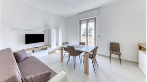 Een moderne woonkamer met een flatscreen televisie, een eettafel met stoelen, een bank en een raam met zonwering.