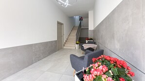 Een modern interieur met een trap, grijs gestoffeerde stoelen en een hanglamp.