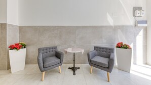 Een moderne kamer met twee grijze fauteuils, een klein rond tafeltje en een witte muur met een grijze accentkleur.