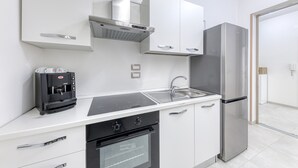 Een moderne keuken met witte kastjes, een roestvrijstalen koelkast, een inbouwoven en een koffieapparaat.