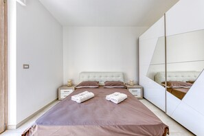 A modern bedroom with a large bed, bedside tables, a mirror, and a wardrobe.