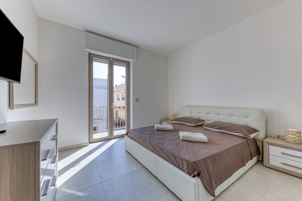 A bedroom with a bed, a TV, a desk, and a balcony.