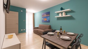 A modern living room with a sofa, a dining table set for two, and a TV mounted on the wall. - Holiday Apartment 'Appartamento A Pigna' with Balcony, Wi-Fi and Air Conditioning (Balestrate)