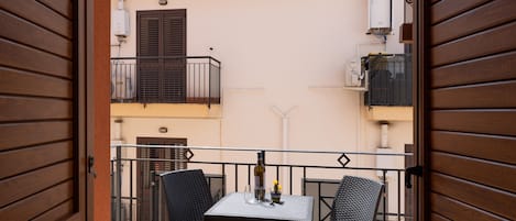 An open balcony with a table and chairs, a window with shutters, and a view of the building's exterior.