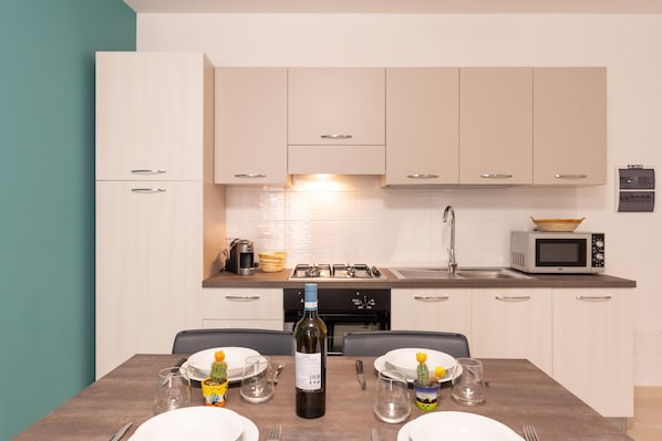Una cocina moderna con armarios blancos, estufa a gas, microondas y una mesa de comedor para dos personas, con copas de vino y platos.