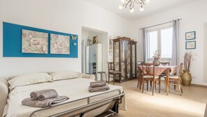 Een slaapkamer met een bed, een eettafel, stoelen, een kast en kunst aan de muren.