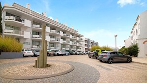 A multi-story residential building with balconies, a paved courtyard, and parked cars. - Apartment 'Golden Ocean' with Shared Pool, Wi-Fi and Air Conditioning (Cabanas de Tavira)