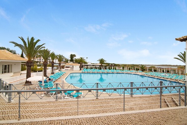 Una gran piscina con sillas azules y palmeras, rodeada por una valla.