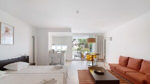 A hotel room with a bed, a sofa, a dining area, and a view of the outdoors. - Apartment 'Golden Ocean' with Shared Pool, Wi-Fi and Air Conditioning (Cabanas de Tavira)