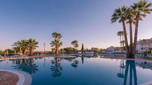 A swimming pool with palm trees and lounge chairs. - Apartment 'Golden Ocean' with Shared Pool, Wi-Fi and Air Conditioning (Cabanas de Tavira)