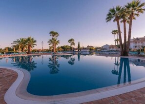 Piscina con palmeras y sillas de descanso.