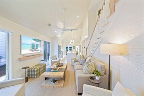 A modern living room with a large window, a ceiling fan, and a staircase.