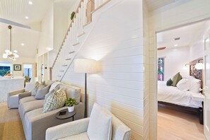 A modern living room with a staircase, a dining area, and a bedroom with a bed and nightstands.